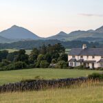 white farmhouse set with a backdrop of trees and mountains.